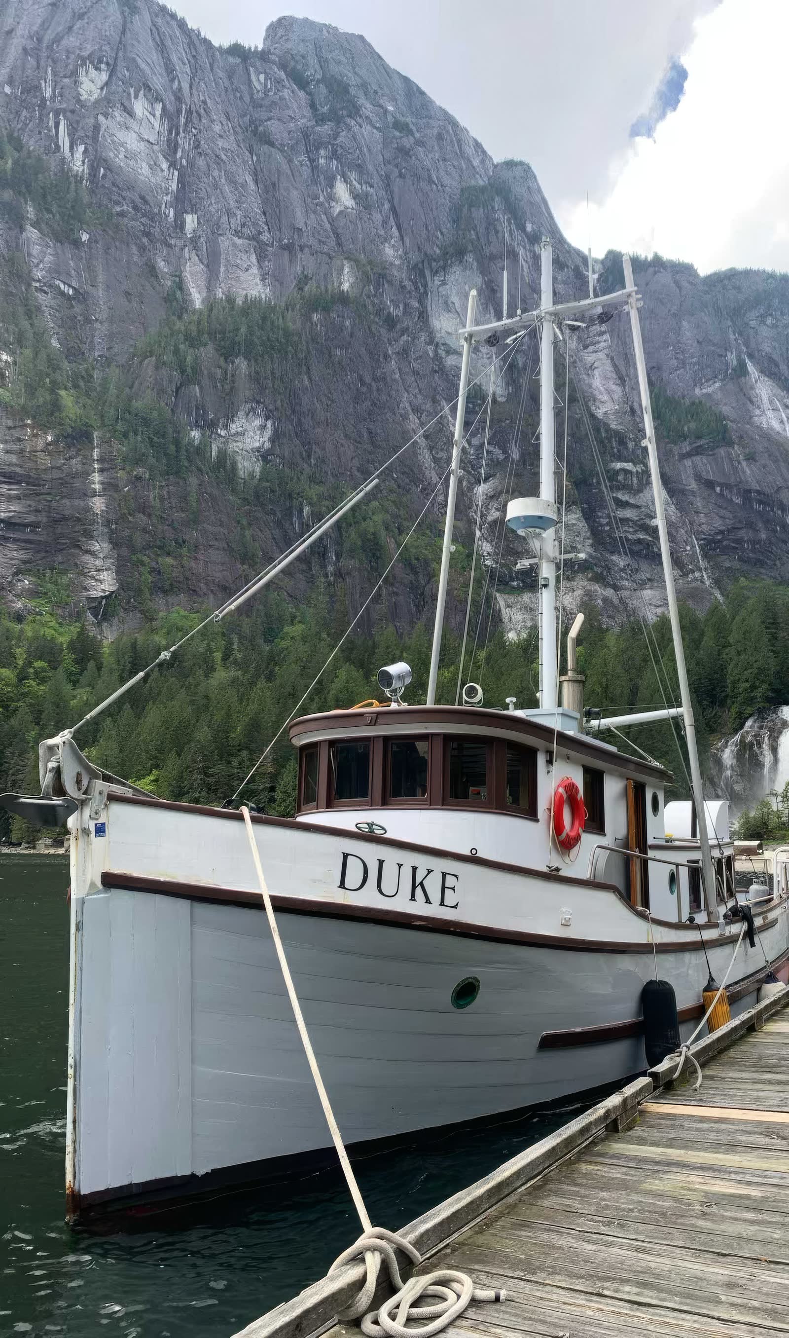 Duke, a white wooden troller with brown trim, tied to a float beneath granite cliffs and a waterfall